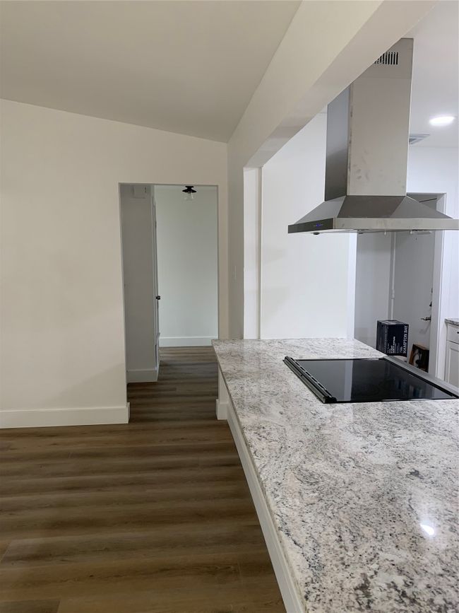 Kitchen featuring ventilation hood, cooktop, dark wood-style flooring, lofted ceiling, and light stone counters | Image 8