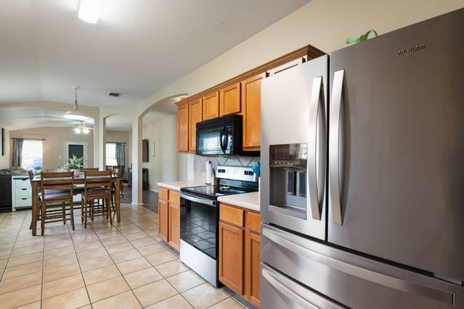 Kitchen with stainless steel appliances, light tile patterned floors, light countertops, backsplash, and brown cabinets | Image 6