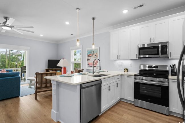 Kitchen with appliances with stainless steel finishes, white cabinetry, light wood-type flooring, ornamental molding, and open floor plan | Image 9