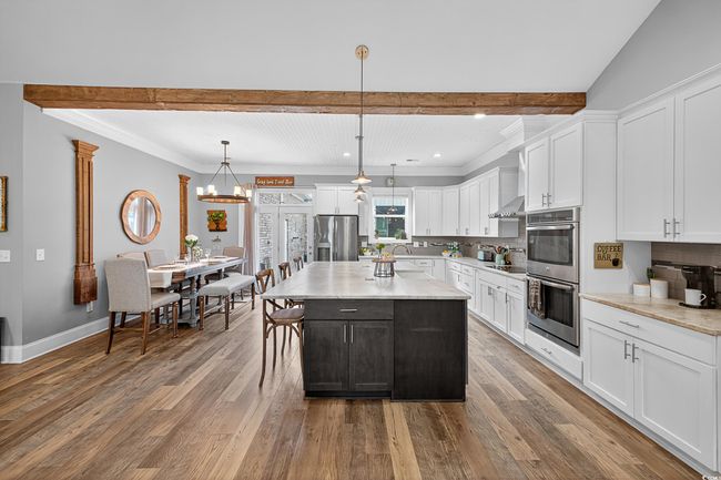 Kitchen featuring stainless steel appliances, backsplash, white cabinetry, wood finished floors, and beamed ceiling | Image 17