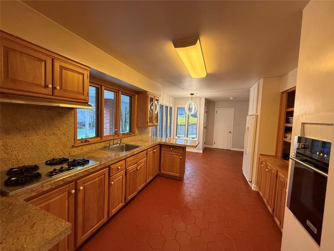 Kitchen featuring a peninsula, stainless steel stovetop, brown cabinetry, wall oven, and a sink | Image 5