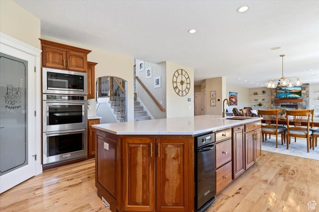 Kitchen with stainless steel double oven, light wood-style flooring, built in microwave, and a kitchen island with sink | Image 16