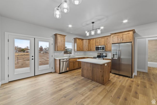 Kitchen with light countertops, light wood finished floors, stainless steel appliances, a kitchen island, and a sink | Image 11