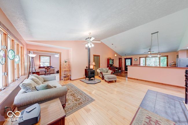 living room featuring a wood stove, ceiling fan, plenty of natural light, wood finished floors, and lofted ceiling | Image 49