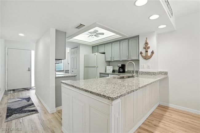 Kitchen featuring freestanding refrigerator, a peninsula, light wood-type flooring, recessed lighting, and light stone counters | Image 13