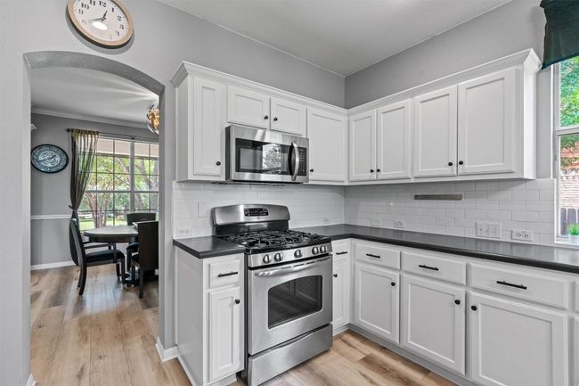 Kitchen featuring stainless steel appliances, dark countertops, white cabinets, and light wood-style floors | Image 12