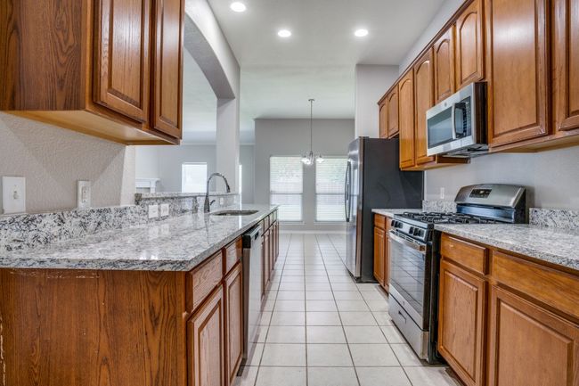 Kitchen featuring stainless steel appliances, a sink, brown cabinetry, light tile patterned floors, and light stone counters | Image 9
