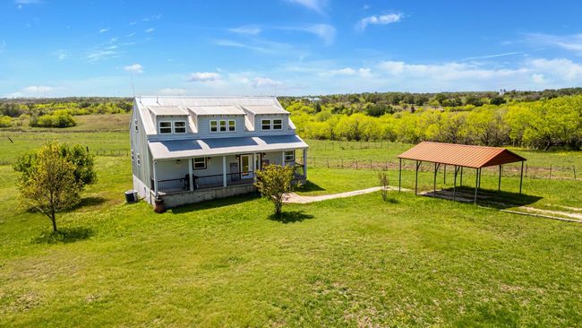 Back of house featuring covered porch, a rural view, central AC unit, a lawn, and a detached carport | Image 5