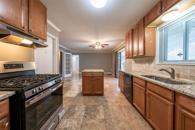 Kitchen with stainless steel gas stove, dishwasher, ornamental molding, under cabinet range hood, and brown cabinetry | Image 11