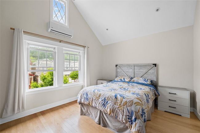 Bedroom featuring a wall unit AC, multiple windows, light wood-style flooring, and high vaulted ceiling | Image 26