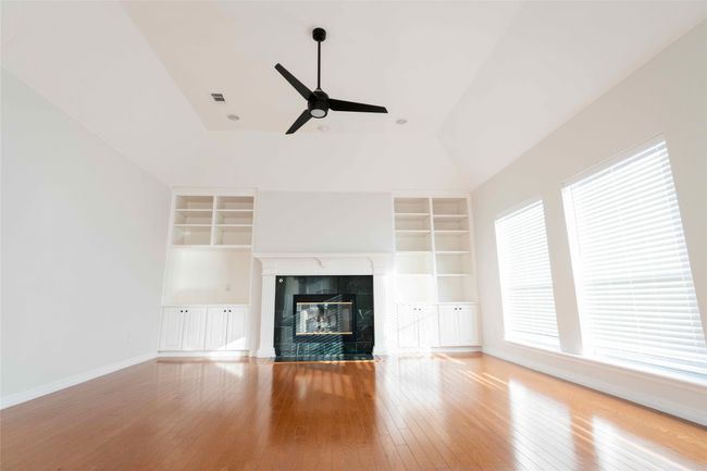 Unfurnished living room featuring built in shelves, vaulted ceiling, a ceiling fan, a fireplace, and hardwood / wood-style flooring | Image 13