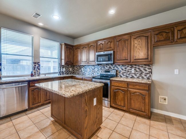 Kitchen featuring visible vents, backsplash, light stone counters, a kitchen island, and appliances with stainless steel finishes | Image 9