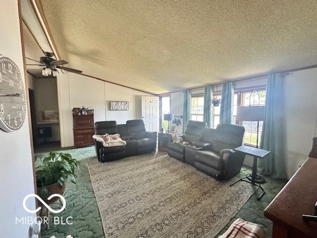 carpeted living room featuring vaulted ceiling, a textured ceiling, and a ceiling fan | Image 4