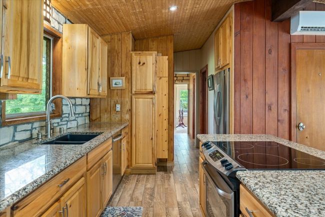 Kitchen with stainless steel appliances, light wood-style flooring, wood walls, wood ceiling, and light stone countertops | Image 12