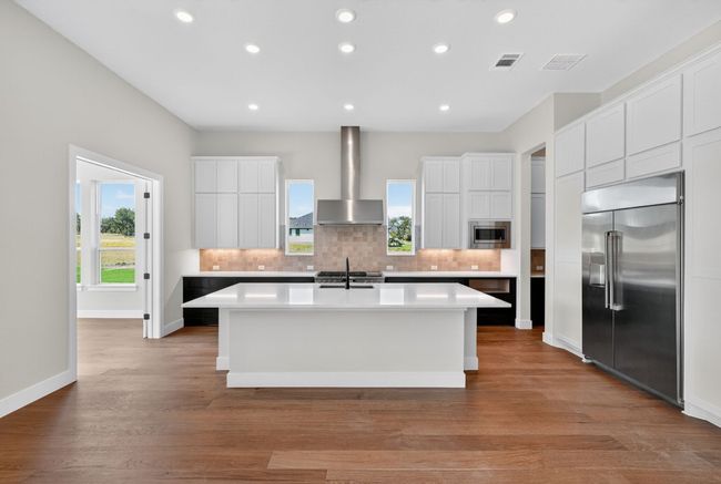 Kitchen featuring tasteful backsplash, white cabinetry, built in appliances, an island with sink, and light wood-style flooring | Image 7