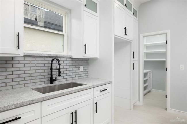 Kitchen featuring a sink, backsplash, light stone counters, white cabinetry, and glass insert cabinets | Image 7