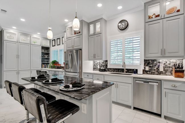 Kitchen with stainless steel appliances, light marble finish flooring, crown molding, decorative backsplash, and a breakfast bar area | Image 13