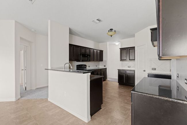 Kitchen with black appliances, backsplash, dark brown cabinetry, dark stone counters, and a peninsula | Image 20