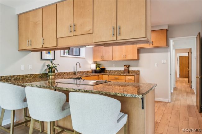 Kitchen featuring dark stone countertops, a sink, stovetop, a peninsula, and a kitchen bar | Image 26