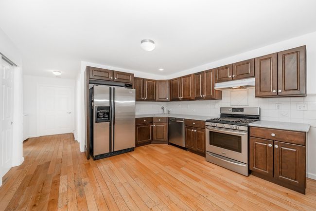 Kitchen featuring light countertops, appliances with stainless steel finishes, light wood-style flooring, under cabinet range hood, and decorative backsplash | Image 6