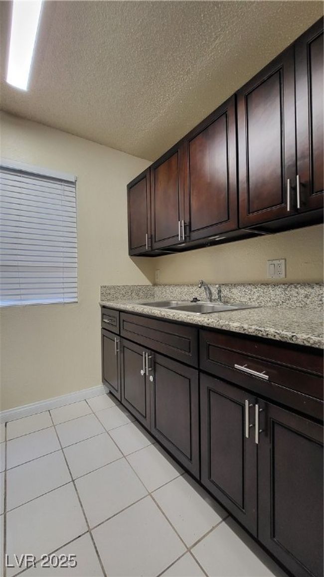 Kitchen with light tile patterned floors, a textured ceiling, a sink, dark brown cabinets, and baseboards | Image 6