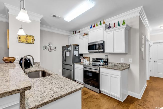 Kitchen featuring appliances with stainless steel finishes, a sink, crown molding, light wood-style flooring, and white cabinets | Image 5