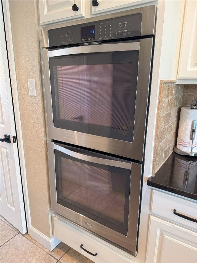 Kitchen view of double oven, tasteful backsplash, white cabinetry, and dark stone countertops. | Image 11