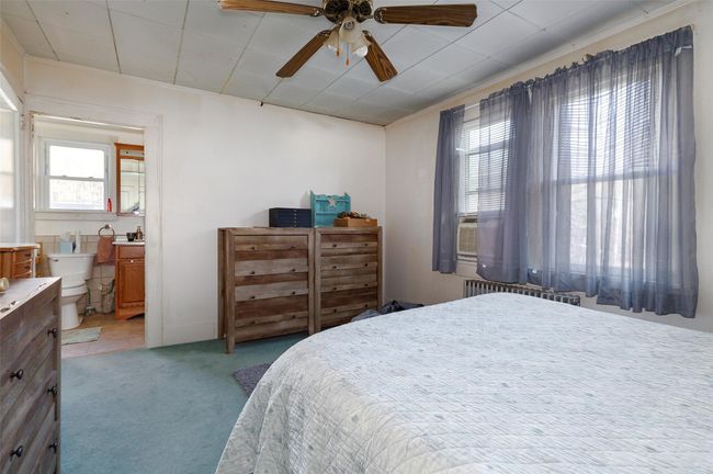 Bedroom featuring light carpet, radiator heating unit, connected bathroom, and ceiling fan | Image 14