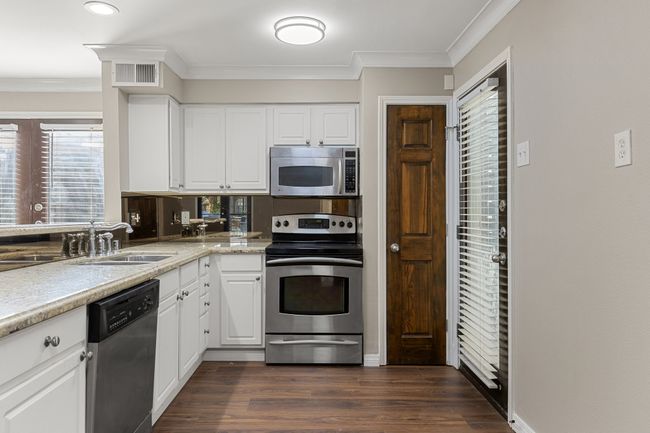 Kitchen with ornamental molding, dark wood-type flooring, visible vents, stainless steel appliances, and a sink | Image 6