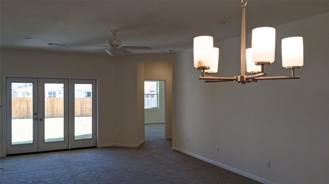 View from dining space with modern chandelier: through the living room to french doors to the covered patio and large back yard. The primary suite is through the doorway to the right and features an art niche at the entrance. | Image 6