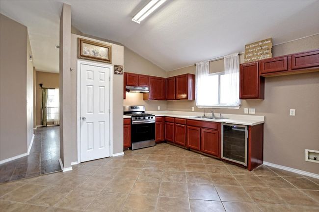 Kitchen featuring stainless steel gas range oven, beverage cooler, a sink, vaulted ceiling, and under cabinet range hood | Image 12