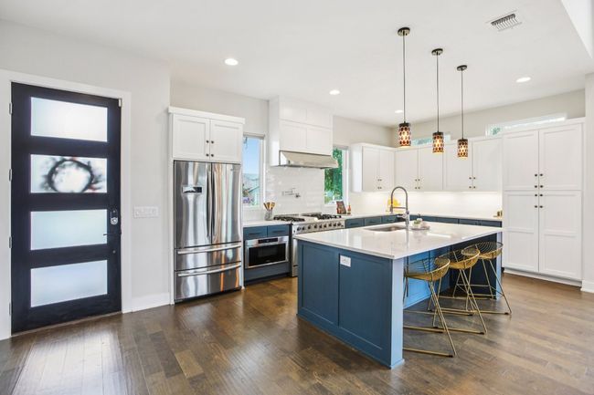 Kitchen featuring appliances with stainless steel finishes, under cabinet range hood, white cabinets, light countertops, and decorative light fixtures | Image 13