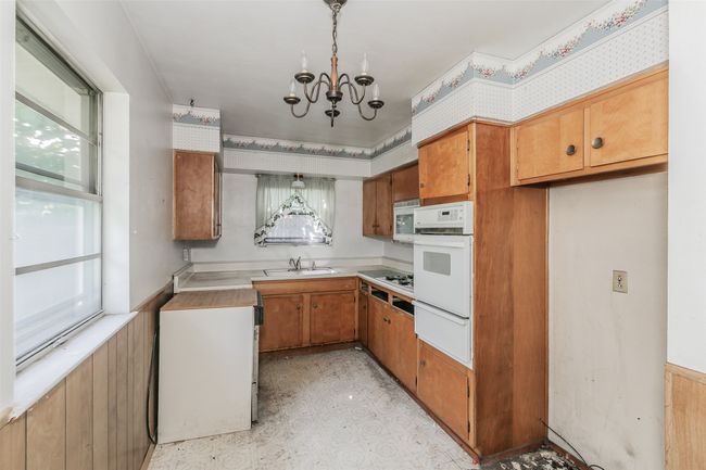 Kitchen featuring white appliances, a warming drawer, brown cabinetry, a chandelier, and light countertops | Image 8