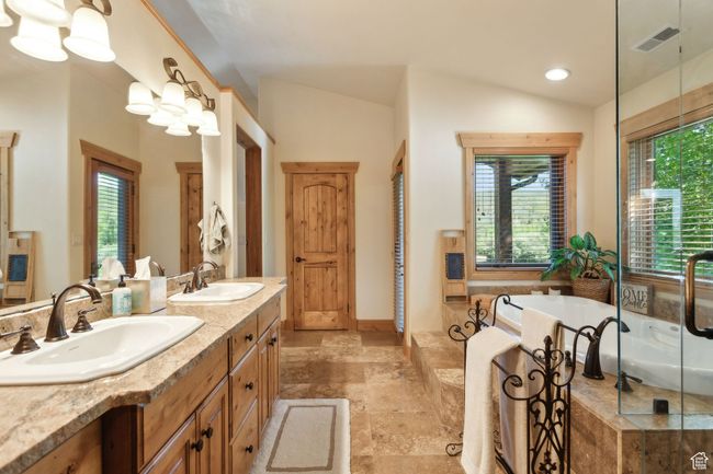 Bathroom featuring double vanity, a bath, vaulted ceiling, and stone finish floors | Image 30