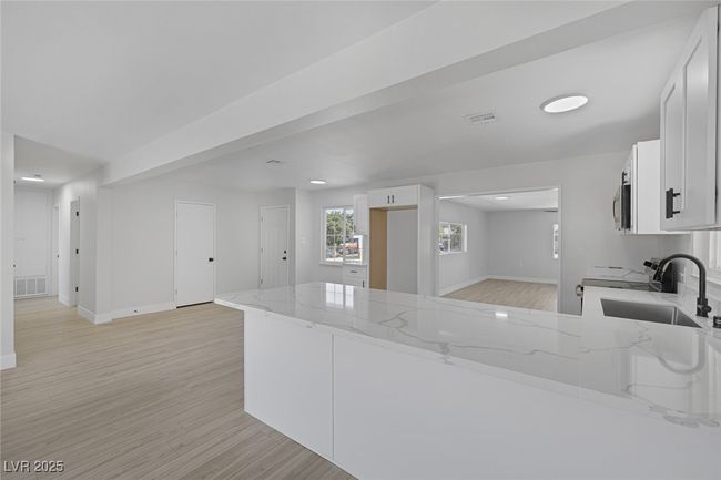 Kitchen with light stone countertops, a peninsula, light wood-type flooring, white cabinetry, and electric stove | Image 9