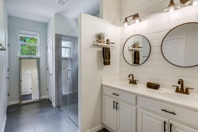 Ensuite bathroom with double vanity, a shower stall, tile patterned flooring, baseboards, and wooden walls | Image 5