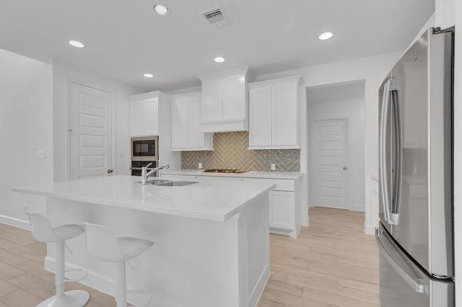 Kitchen featuring stainless steel appliances, light wood-style floors, light countertops, tasteful backsplash, and white cabinetry | Image 8