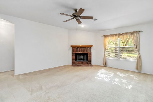 Unfurnished living room featuring a ceiling fan, arched walkways, a brick fireplace, carpet, and baseboards | Image 13