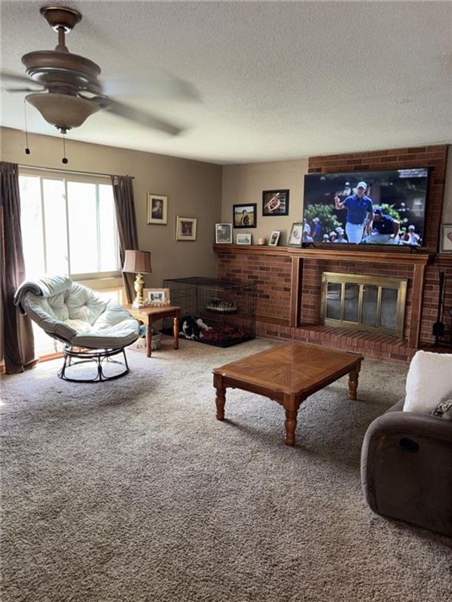 Carpeted living area featuring a textured ceiling, a ceiling fan, and a brick fireplace | Image 4