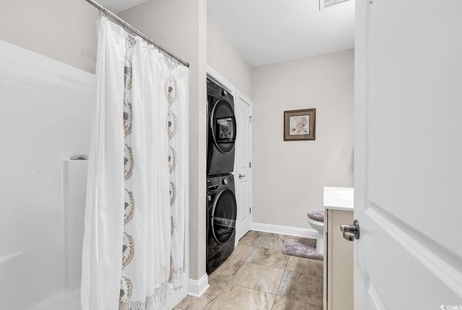 Bathroom featuring stacked washer and clothes dryer, vanity, toilet, marble look tile flooring, and baseboards | Image 9