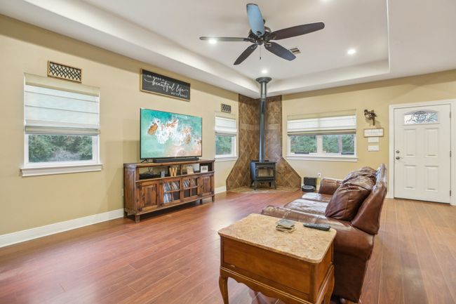 Living room featuring a raised ceiling, wood-type flooring, a healthy amount of sunlight, and a wood stove | Image 4