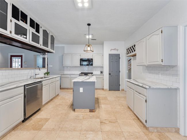 Kitchen featuring appliances with stainless steel finishes, decorative backsplash, glass insert cabinets, a kitchen island, and light stone countertops | Image 10