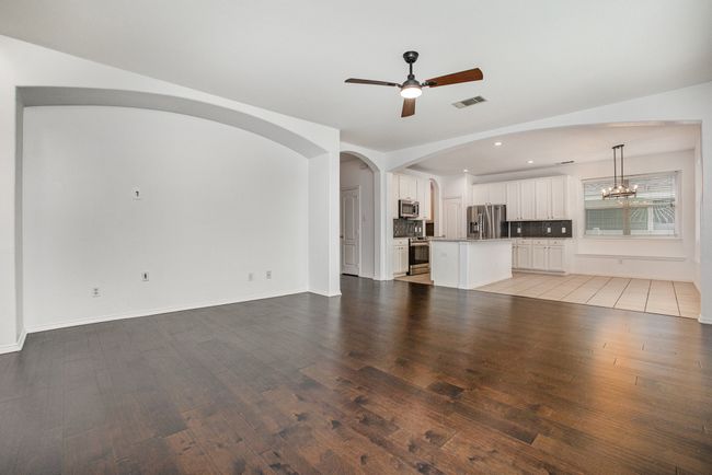 Unfurnished living room featuring ceiling fan with notable chandelier, visible vents, wood-style flooring, and recessed lighting in kitchen | Image 7