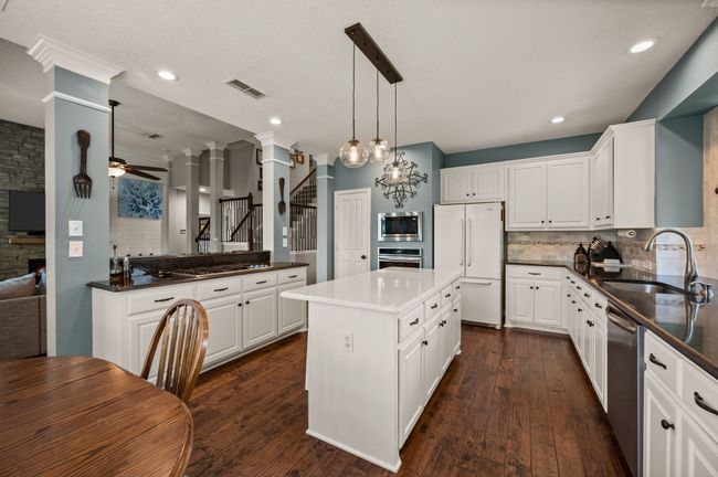 Kitchen featuring white cabinets, tasteful backsplash, a ceiling fan, stainless steel appliances, and hanging light fixtures | Image 13