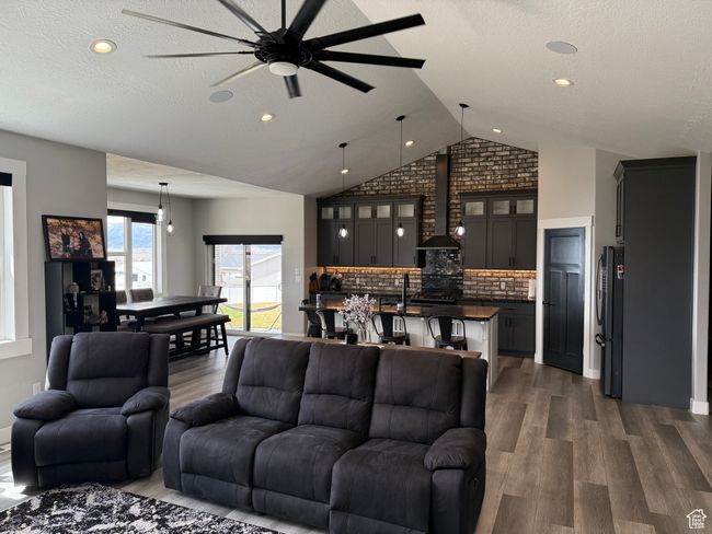 Living area featuring dark wood-style flooring, a textured ceiling, vaulted ceiling, and ceiling fan | Image 5