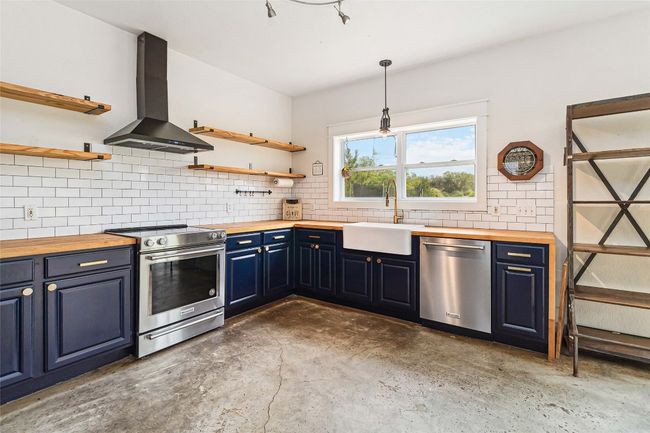 Kitchen with wooden counters, appliances with stainless steel finishes, open shelves, a sink, and wall chimney exhaust hood | Image 13