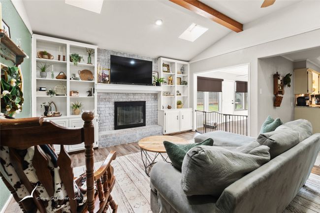 Living room with built in features, a brick fireplace, light wood finished floors, and lofted ceiling with skylight | Image 5