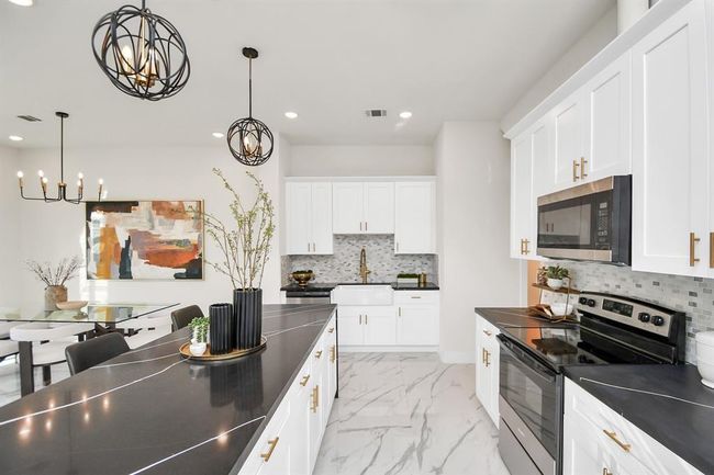 Chef's dream kitchen; upgraded waterfall island with Quartz counters, farmhouse sink with upgraded faucet, handles on the cabinetry, crown molding on the cabinets and luxurious pendant lights- this is your DREAM kitchen. All selections made by an interior designer. | Image 7