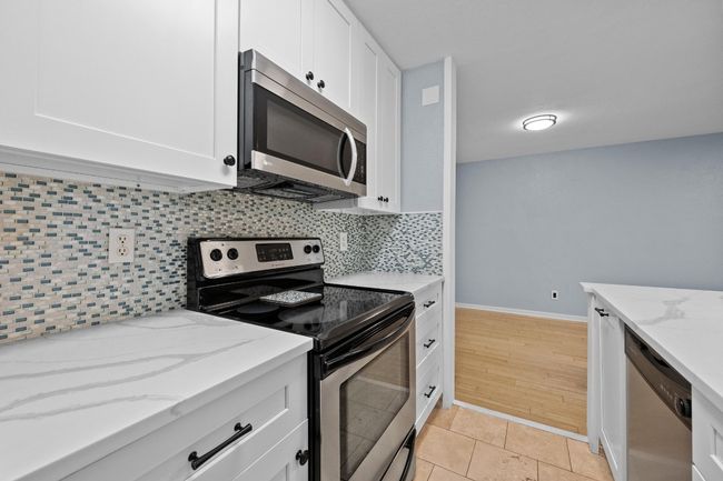 Kitchen featuring stainless steel appliances, decorative backsplash, white cabinetry, light stone counters, and baseboards | Image 4