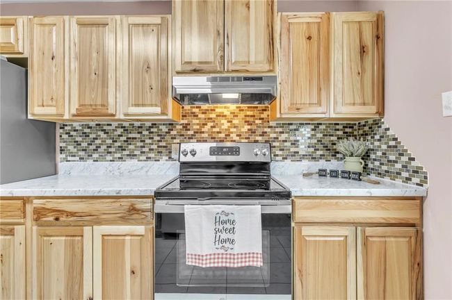Kitchen with backsplash, electric range, light brown cabinetry, and under cabinet range hood | Image 22